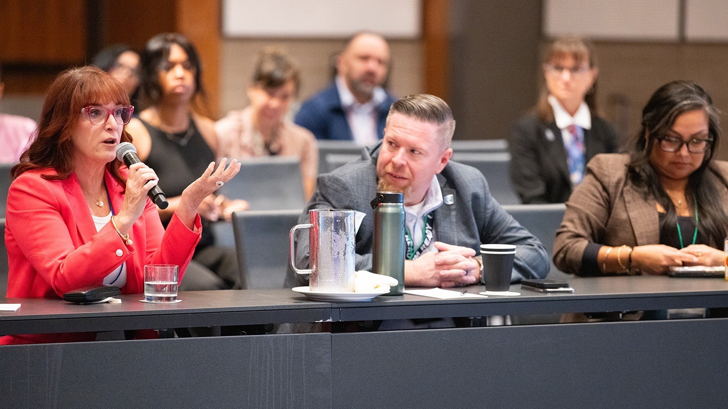 woman in red speaking with a white man and Latina woman seated next to her